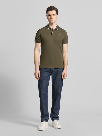Męski model nosi Slim Fit Poloshirt mit Kontraststreifen von Geox, mieszanka bawełny, krój slim fit, kołnierzyk polo, krótka listwa guzikowa, paski w kontrastowym kolorze, długość tyłu w rozmiarze M: 69 cm, całopostaciowy widok z przodu.