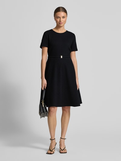 Vrouwenmodel draagt knielangens jurk uit katoenmix met structuurpatroon van Marc Cain, A-lijn, getailleerde pasvorm, logodetail, afneembare stoffen riem, met korte mouwen, ronde hals, zwarte kleur; volledige lichaamsaanzicht van voren.