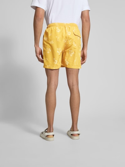 Männermodel trägt Badehose mit Eingrifftaschen von Closed in Gelb mit weißen Prints, elastischer Bund, Ganzkörperansicht Rückansicht