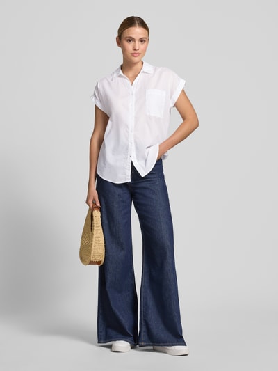 Frauenmodel trägt Relaxed Fit Bluse mit Brusttasche Modell 'DORA' von Soyaconcept aus reiner Baumwolle, Hemdblusenkragen, Kappärmel, Rückenlänge 66 cm, Ärmel 6 cm, weiße Farbe, leicht strukturierte Oberfläche, Ganzkörperansicht von vorne.
