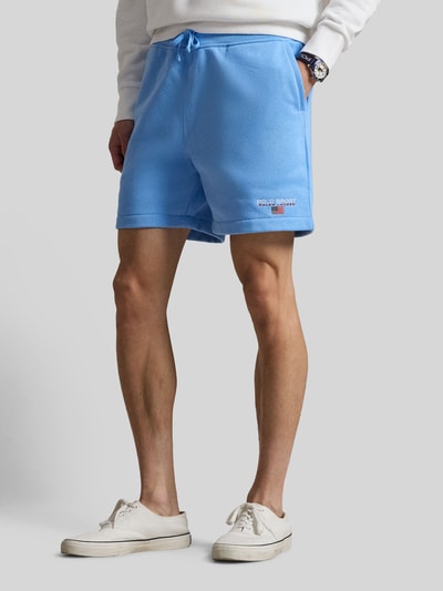 Męski model nosi Regular Fit Sweatshorts aus Baumwoll-Mix von Polo Ralph Lauren, kolor jasnoniebieski, materiał sweat, aplikacja z logo, elastyczny pas z troczkiem, kieszenie z boku i tylna, widok całej sylwetki z przodu.