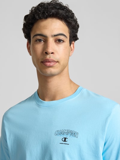 Männermodel trägt T-Shirt mit Logo und Rundhalsausschnitt von CHAMPION aus Reine Baumwolle, Regular-Fit in Hellblau, Nahaufnahme Oberkörper. Rückenlänge bei Größe M: 61 cm.