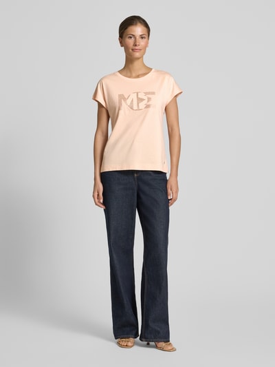 Frauenmodel trägt Regular Fit T-Shirt mit Ziersteinbesatz von monari in Pfirsichton aus Baumwoll-Modal-Mix, Rundhalsausschnitt, Rückenlänge bei Größe 36: 57 cm, Ganzkörperansicht von vorne.