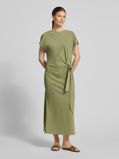 Frauenmodel trägt Midikleid aus reiner Baumwolle von Scotch & Soda in Grün mit Knoten-Detail, taillierte Passform, Ganzkörperansicht von vorne.