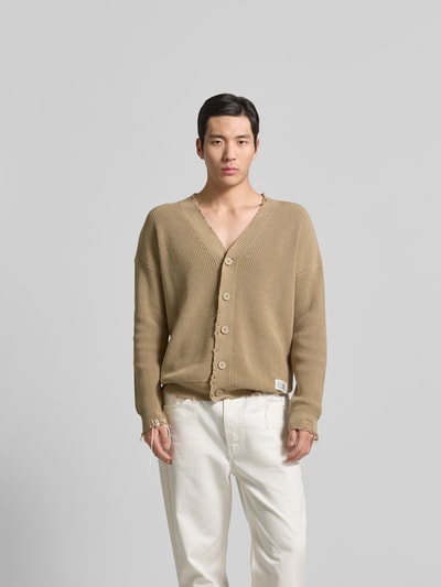 Männermodel trägt Regular Fit Cardigan im Used-Look von MM6 Maison Margiela in Beige, reine Baumwolle, Knopfleiste, Logo-Detail, Ganzkörperansicht von vorne.