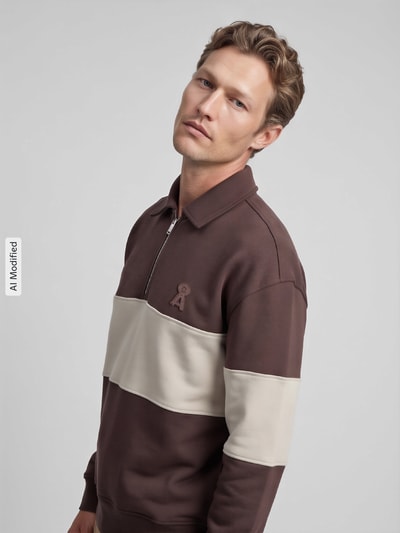 Männermodel trägt Relaxed Fit Sweatshirt aus reiner Baumwolle von ARMEDANGELS in Braun mit beigem Streifen, dezente Textur, Nahaufnahme Oberkörper, KI-modifiziertes Bild.