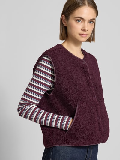 Modelka nosi kamizelkę z futerka o kroju regular fit, model 'Vera' od JJXX z okrągłym dekoltem, wpuszczanymi kieszeniami i listwą guzikową, widoczne jednorodne kolory i wyrazista tekstura futerka, widok na górną część ciała z przodu.