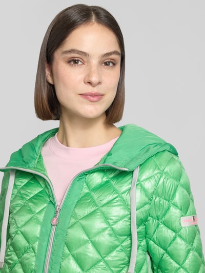 Frauenmodel trägt Regular Fit Jacke in Stepp-Optik Modell 'YOSIE' von Frieda & Freddies in Grün mit Kapuze, Eingrifftaschen, Reißverschluss, Logo-Applikation, elastische Ärmelabschlüsse, Nahaufnahme Oberkörper. Rückenlänge bei Größe 36: 61 cm, Schulterbreite 46 cm, Brustweite 49 cm, Ärmellänge 60 cm.