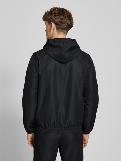 Männermodel trägt schwarzen Regular Fit Tracksuit mit Logo-Stitching Modell 'Carson' von SERGIO TACCHINI, elastische Abschlüsse, Kapuze, Reißverschluss, Eingrifftaschen, Rückansicht, Materialstruktur glatt.