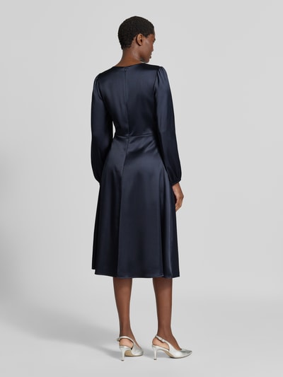 Vrouwenmodel draagt donkerblauwe midi-jurk van satijn met druppelvormige hals van Christian Berg Woman Selection, elastische materiaalmix, getailleerde pasvorm, met lange mouwen, ruglengte bij maat 36 112 cm, borstwijdte 44 cm, mouwlengte 55 cm, Ganzkörperansicht Rückansicht.