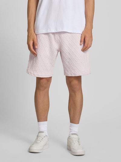 Männermodel trägt Relaxed Fit Sweatshorts mit Strukturmuster Modell 'Jovren' von Pegador in Hellrosa, Baumwoll-Mix, Ganzkörperansicht von vorne.