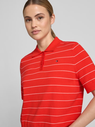 Frauenmodel trägt Regular Fit Pullover aus reiner Baumwolle mit Polokragen von Tommy Hilfiger für Damen in Rot mit weißen Streifen, Nahaufnahme Oberkörper.
