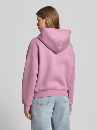 Frauenmodel trägt Sweatjacke mit Logo und Känguru-Tasche von Review in Rosa, aus Baumwoll-Mix, Relaxed-Fit, Kapuze, Reißverschluss, Ganzkörperansicht Rückansicht.