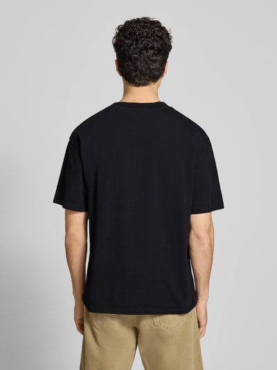 Männermodel trägt Herren T-Shirt mit Motiv-Print Modell 'POSITIVE CHAOS' von Edwin in Schwarz, Relaxed-Fit, Reine Baumwolle, Rückenlänge 70 cm, Ganzkörperansicht Rückansicht.