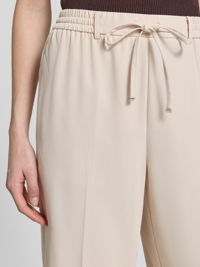 Frauenmodel trägt Wide-Leg-Pants mit elastischem Bund und Kordelzug, angedeutete Gesäßleistentasche, Modell 'Cevil ease' von Someday, Damen, beige, Schlupfhosen-Design, Nahaufnahme Oberkörper. Bundweite 36 cm, Innenbeinlänge 77 cm, Größe 36.