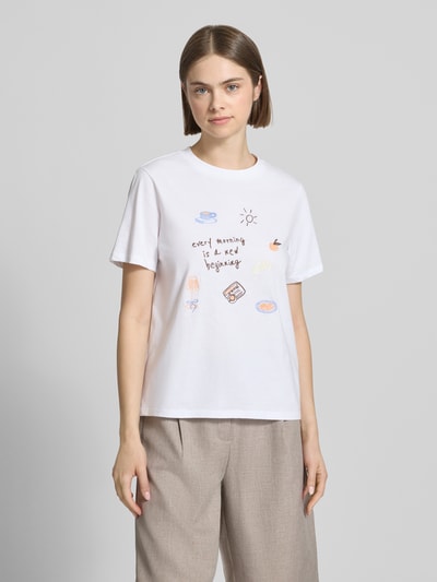 Frauenmodel trägt Damen T-Shirt von Pieces, Modell 'Regular Fit T-Shirt aus reiner Baumwolle Modell 'GAK', Optik: Unifarben, Passform: Regular-Fit, Applikation: Stickerei, Rundhals-Ausschnitt, Ärmelform: Kurzarm, Material: Reine Baumwolle, helles Weiß mit farbigen Stickereien, glatte Textur, Ganzkörperansicht von vorne.
