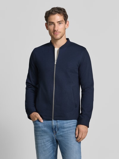 Męski model nosi Slim Fit Sweatjacke mit Stehkragen od Lindbergh, Mieszanka materiałów z dodatkiem streczu, krój slim fit, stójka, zamek błyskawiczny, boczne wpuszczane kieszenie, długość tyłu w rozmiarze M: 67 cm, długość rękawów w rozmiarze M: 66 cm, ciemnoniebieski kolor, gładka tekstura, Ganzkörperansicht von vorne.