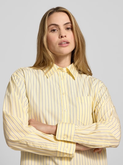 Frauenmodel trägt Relaxed Fit Bluse mit Brusttasche von Gant in Gelb mit feinen Streifen, reine Baumwolle, Hemdblusenkragen, Nahaufnahme Oberkörper.