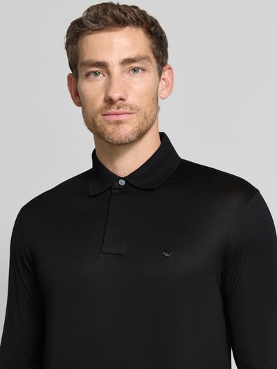 Männermodel trägt schwarzes Slim Fit Poloshirt aus Lyocell-Mix von Emporio Armani mit Polokragen, Kurzarm, feine Textur, Nahaufnahme Oberkörper.