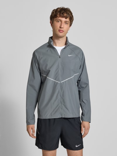 Männermodel trägt Regular Fit Jacke mit Stehkragen Modell 'Miler' von NIKE TRAINING in Grau mit Logo-Print und Reißverschluss, Ganzkörperansicht von vorne. Rückenlänge 67 cm, Ärmellänge 64 cm.