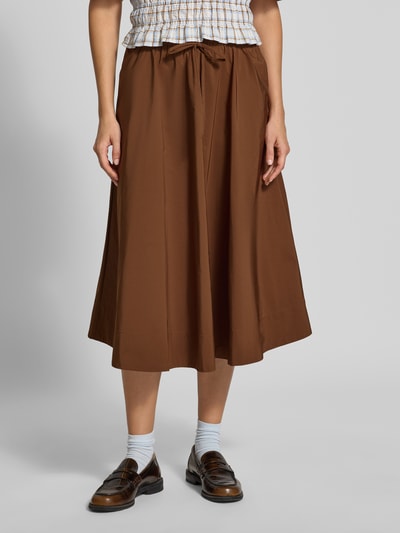 Frauenmodel trägt A-Linien Midi-Rock mit elastischem Bund Modell 'KEELY2' von Essentiel Antwerp in Braun, glatte Textur, Nahaufnahme Unterkörper. Damen Midi-Rock von Essentiel Antwerp.