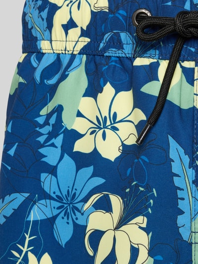 Produktfoto, Badeshorts mit Gesäßtasche Modell 'BHRADBORNE TROPICAL' von Blend, florales Muster in Blau und Gelb, Textur aus glattem Stoff, elastischer Bund mit schwarzem Kordelzug, seitliche Eingrifftasche und Klett-Gesäßtasche, Label-Patch erkennbar