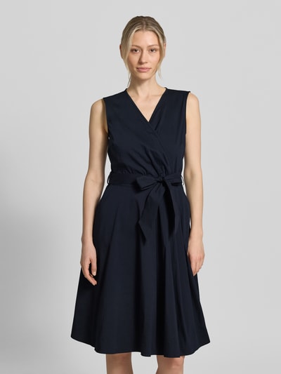 Frauenmodel trägt Kleid mit V-Ausschnitt in Wickel-Optik von More & More aus Baumwoll-Mix, Tailliert, Ärmelloses-Design, Taillenband, Ganzkörperansicht von vorne