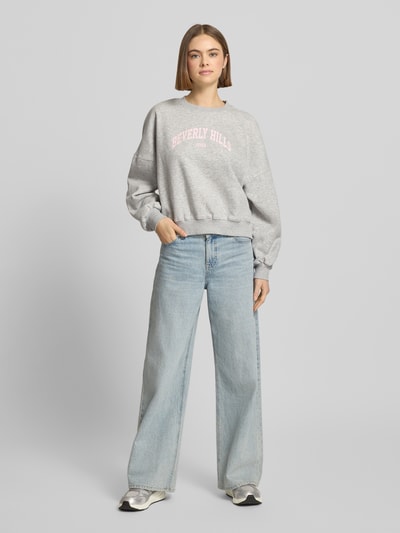 Frauenmodel trägt Sweatshirt mit Label-Print und Rundhalsausschnitt von Review aus Baumwoll-Mix im Relaxed-Fit, grau, Ganzkörperansicht von vorne.