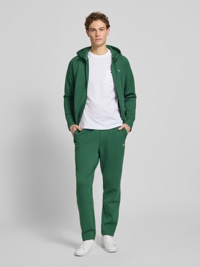 Męski model nosi zielone Tapered Sweatpants mit Baumwoll-Anteil od Lacoste Sport, gładka faktura, logo, przód, cała sylwetka.