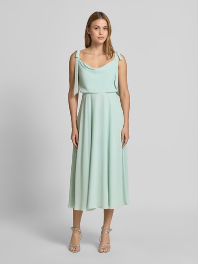 Frauenmodel trägt Knielanges Cocktailkleid mit Zierschleifen von Jake*s Cocktail in Mintgrün, Taillierte Passform, Ärmelloses-Design, blickdichter Unterrock, fließender Stoff, Ganzkörperansicht von vorne.