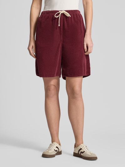 Modelka nosi Shorts mit elastischem Bund Modell 'PADOW' od American Vintage, bordowy, miękka wiskoza, luźny krój, widok całej sylwetki z przodu. Szerokość w rozmiarze S: 37 cm, długość wewnętrzna nogawki w rozmiarze S: 20 cm, tylna kieszeń, tunel na sznurek.