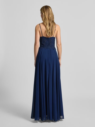 Modelka nosi Regular Fit Abendkleid mit Strasssteinbesatz od Mascara, obszycie koronką, krój regular fit, lekka linia a, cienkie ramiączka, obszycie z kamieni stras, półprzezroczysty materiał, wszyty zamek błyskawiczny, długość tyłu w rozmiarze 36: 17 cm, szerokość klatki piersiowej w rozmiarze 36: 34 cm, całkowity widok z tyłu.
