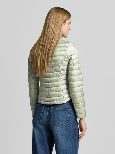 Frauenmodel trägt Steppjacke mit Stehkragen von Gil Bret in hellem Grün, Körpernahe Passform, Rückenansicht, Reißverschlusstaschen, Zweiwege-Reißverschluss, Rücklänge 56 cm, Schulterbreite 39 cm, Brustweite 47 cm, Ärmellänge 66 cm, Größe 36, glatte Oberfläche, dezente Steppnähte, Ganzkörperansicht Rückansicht.