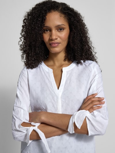 Frauenmodel trägt Regular Fit Bluse mit Tunika-Ausschnitt von Christian Berg Woman aus weißer Baumwolle, sichtbarer Tunnelzug an 3/4-Arm, Nahaufnahme Oberkörper.