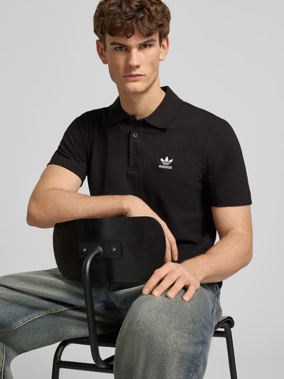 Männermodel trägt Regular Fit Poloshirt mit Logo-Stitching von adidas Originals in Schwarz, reine Baumwolle, Nahaufnahme Oberkörper.