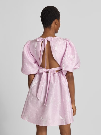 Frauenmodel trägt Cocktailkleid mit Puffärmeln Modell 'NOEALLA' von YAS in zartem Rosa, A-Linie, Strukturmuster, Ganzkörperansicht Rückansicht.