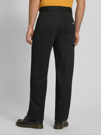 Männermodel trägt Loose Straight Fit Hose mit Bügelfalten von Dickies in Schwarz aus Material-Mix mit Baumwoll-Anteil, Eingrifftaschen, Ganzkörperansicht Rückansicht.