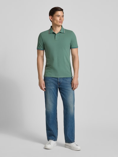 Männermodel trägt Slim Fit Poloshirt mit Kontraststreifen Modell 'Brice' von Sundek, grüner Baumwoll-Elasthan-Mix, Ganzkörperansicht von vorne.