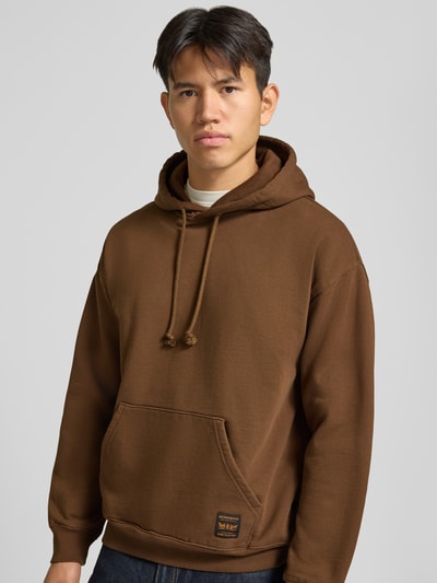 Männermodel trägt Regular Fit Hoodie aus Baumwoll-Mix von Levi's® in Braun mit Kängurutasche, glatte Oberfläche, Nahaufnahme Oberkörper.