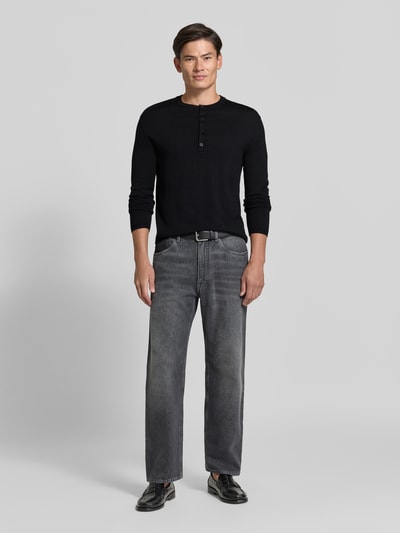 Männermodel trägt Strickpullover mit Henley-Kragen von DRYKORN, reine Baumwolle, schwarz, gerader Schnitt, Ganzkörperansicht von vorne.