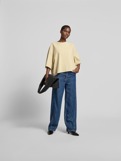 Frauenmodel trägt Damen T-Shirt mit Rundhalsausschnitt von black palms in Reine Baumwolle, Relaxed-Fit, Halbarm, Rückenlänge 55 cm, Farbton Creme, kombiniert mit blauer Jeans, Ganzkörperansicht von vorne.