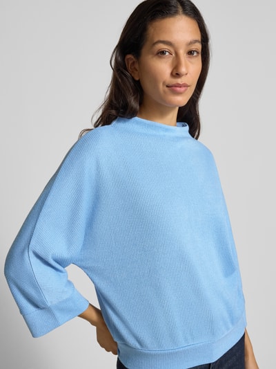 Frauenmodel trägt Longsleeve mit 3/4-Ärmel Modell 'Sagida' von Opus im hellblauen Material-Mix mit Viskose-Anteil, lockerer Schnitt, Stehkragen, gerippte Abschlüsse, Rückenlänge bei Größe 36: 60 cm, Nahaufnahme Oberkörper.