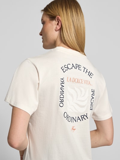 Männermodel trägt damski t-shirt Regular Fit T-Shirt aus reiner Baumwolle Modell 'VINTAGE TEE_25' von HUGO w kolorze kremowym z nadrukiem na plecach, damski t-shirt od HUGO. Ganzkörperansicht Rückansicht.