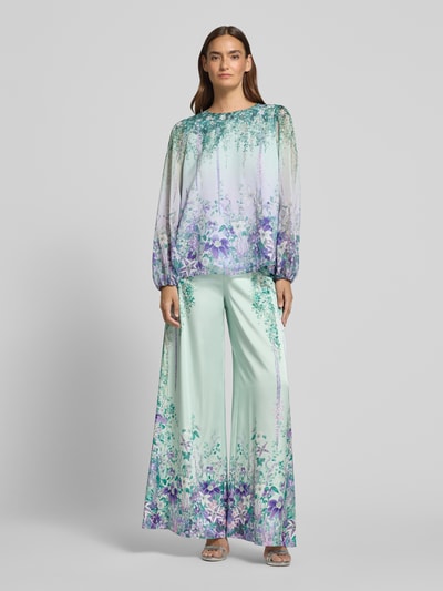 Frauenmodel trägt Regular Fit Bluse mit Rundhalsausschnitt von Marc Cain im schimmernden Allover-Look mit rückseitigem Knopfverschluss, Ganzkörperansicht von vorne. Rückenlänge bei Größe 36: 60 cm, Ärmellänge bei Größe 36: 64 cm.