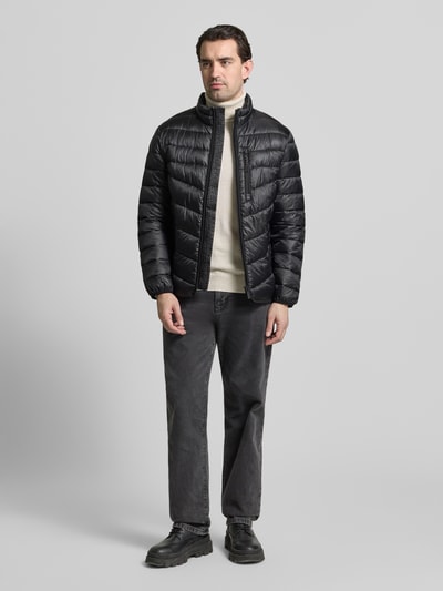 Męski model nosi Regular Fit Steppjacke mit Stehkragen von Tom Tailor, czarna, pikowana, stójka, długi rękaw, elast. ściągacze, wodoodporna, boczne i piersiowa kieszeń na zamek, widok całej sylwetki z przodu.
