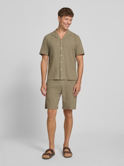 Männermodel trägt Resort Fit Freizeithemd aus reiner Baumwolle von s.Oliver RED LABEL in hellem Oliv, Kurzarm, lockere Passform, Ganzkörperansicht von vorne.