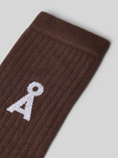 Produktfoto, braune Socken aus Baumwoll-Mix Modell 'SAAMUS' von ARMEDANGELS mit gerippter Textur und weißem Logo auf grauem Hintergrund