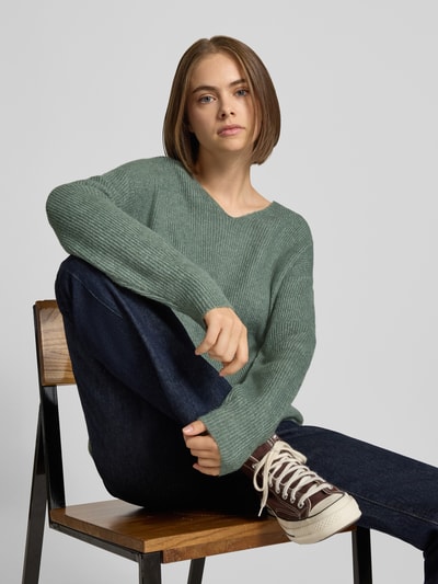 Frauenmodel trägt Regular Fit Pullover mit V-Ausschnitt Modell 'CAMILLA' von ONLY, grün, grob gestrickt, kombiniert mit Jeans, Nahaufnahme Oberkörper, Damen Pullover von ONLY.