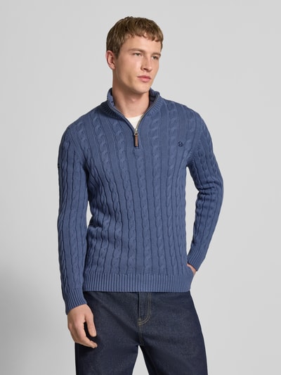 Männermodel trägt Strickpullover aus reiner Baumwolle von Superdry in Blau mit Zopfmuster, Troyer-Kragen, eng anliegender Passform, Label-Detail, gerippte Abschlüsse, Rückenlänge 70 cm, Ärmellänge 71 cm, Ganzkörperansicht von vorne.