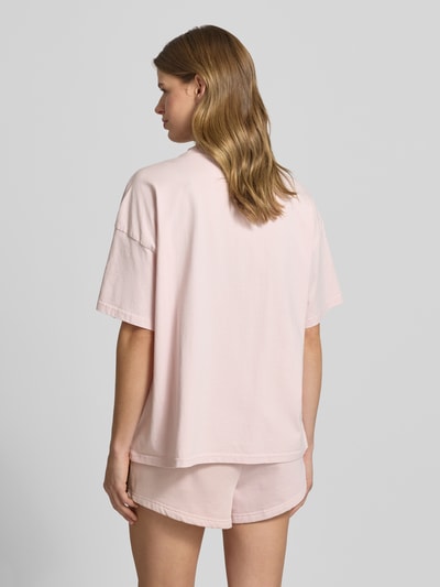 Frauenmodel trägt Oversized Fit Damen T-Shirt Modell 'BRACY' von Pegador aus Reine Baumwolle in zartem Rosa mit Label-Stitching, Rückenlänge bei Größe S 63 cm, Ganzkörperansicht Rückansicht.